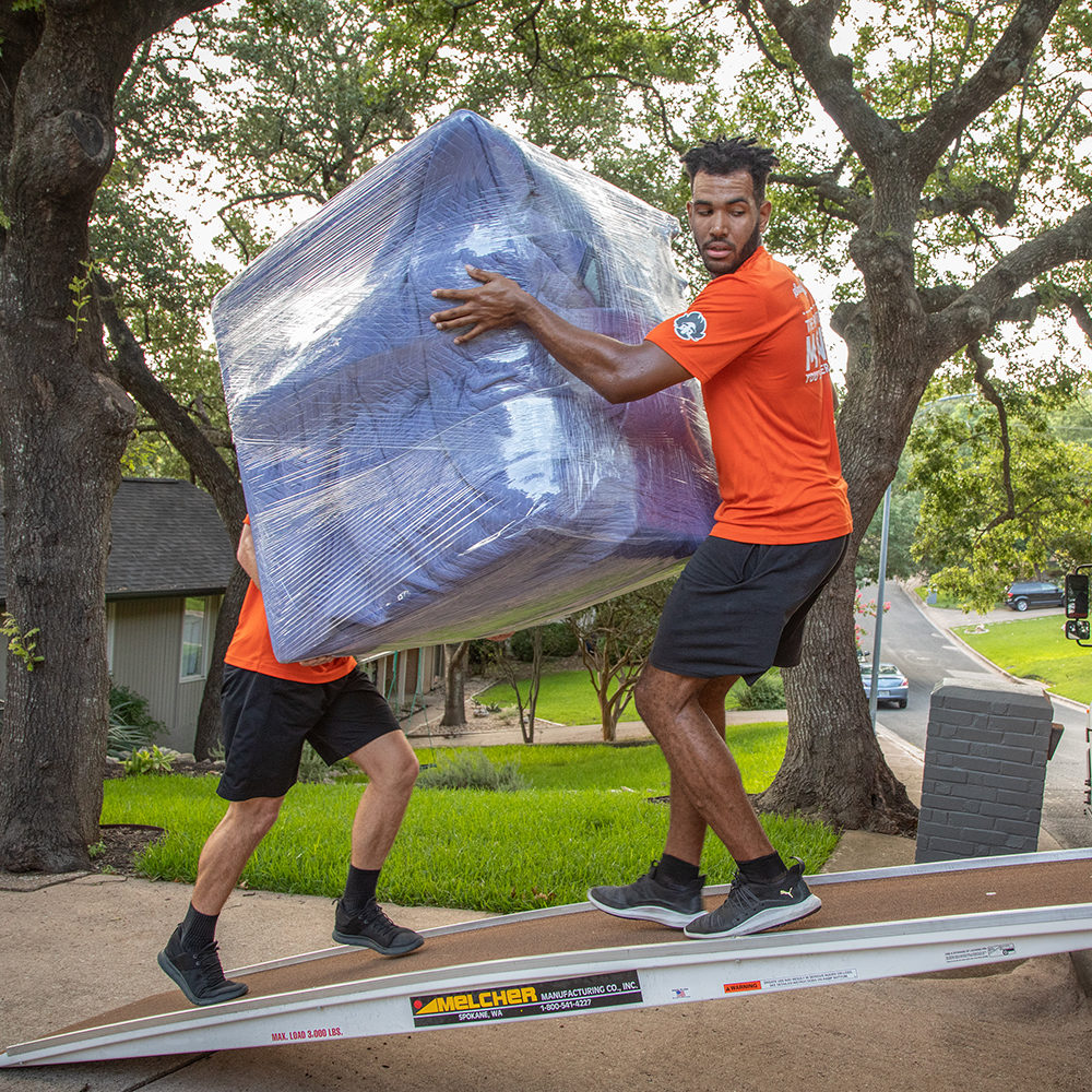 Two Einstein movers load a large object into a moving truck