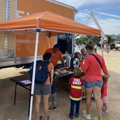 Movers outside a tent in front of a big orange moving truck.