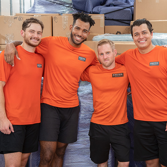 Four Einstein movers pose in front of a stack of boxes.