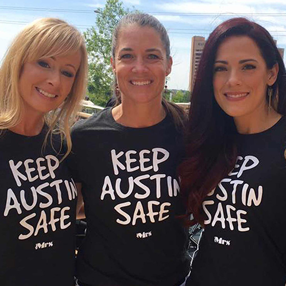 Three woman smile while wearing Keep Austin Safe t-shirts