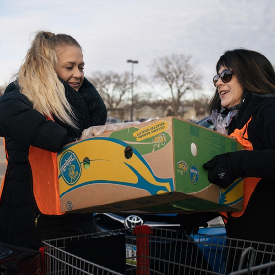 Two female volunteers carry a box of bananas