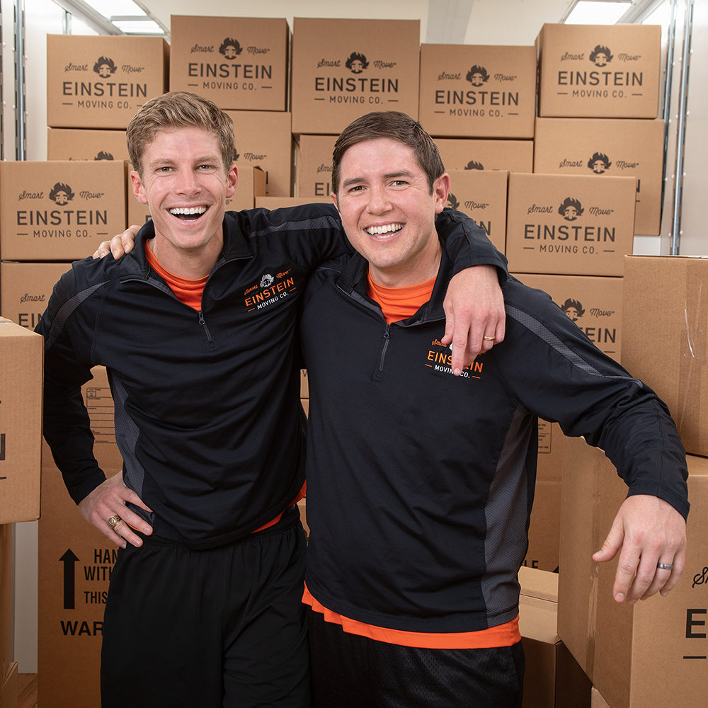 Cameron Brown and Paul Morin pose in front of a stack of Einstein's cardboard moving boxes