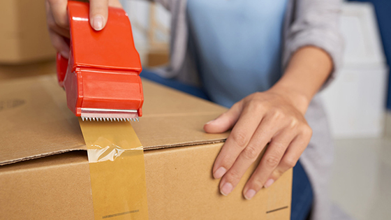 Close-up view of unrecognizable woman sealing cardboard box with adhesive tape while preparing for moving out