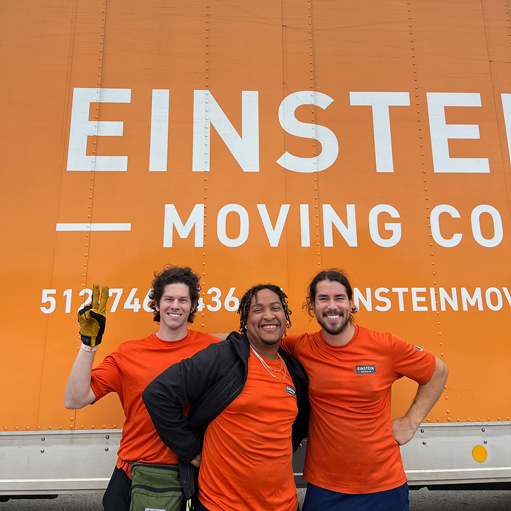 Three members from the Leander team smiling for a photo in front of their moving truck.
