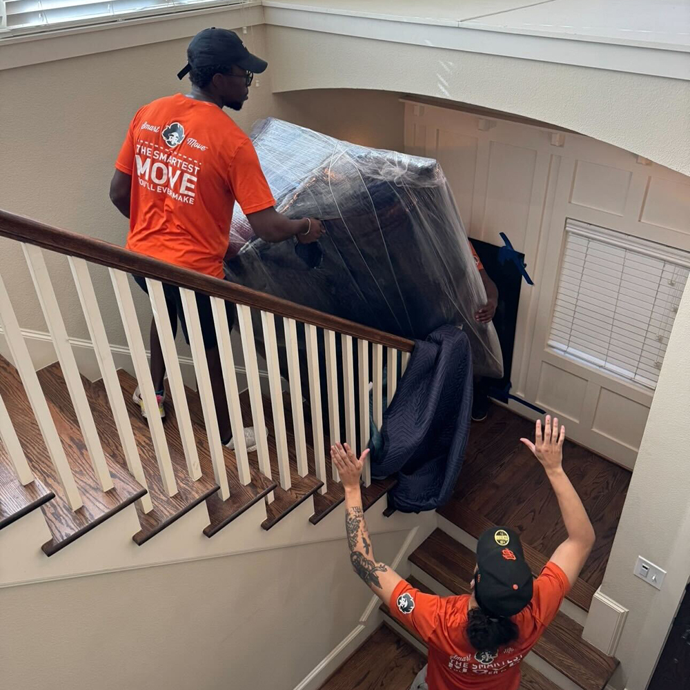 Three movers carefully carrying a couch down a staircase.