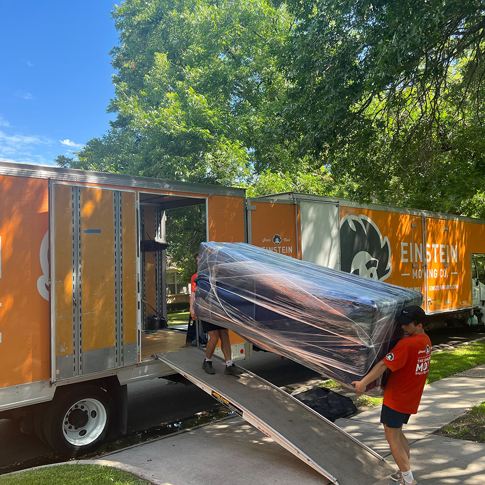 Two men carrying a large piece of furniture out of the moving truck.