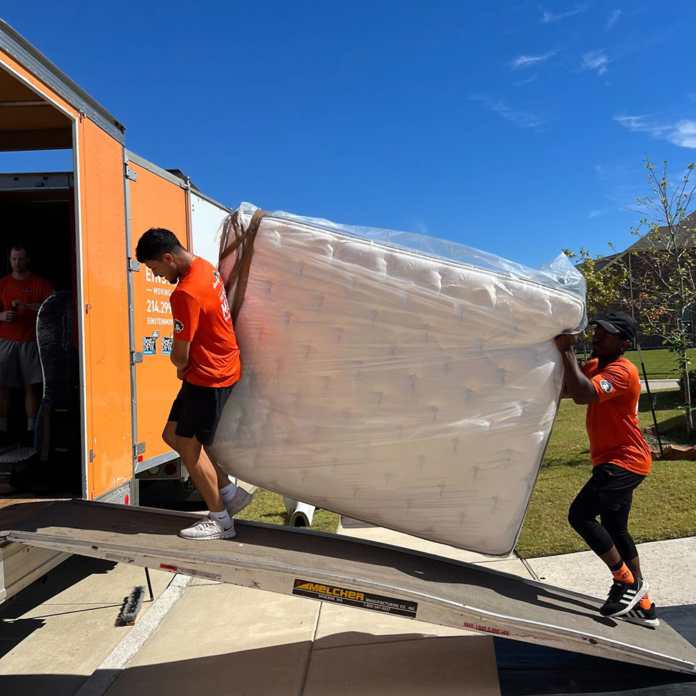 Two men carrying a mattress with protection into moving truck.