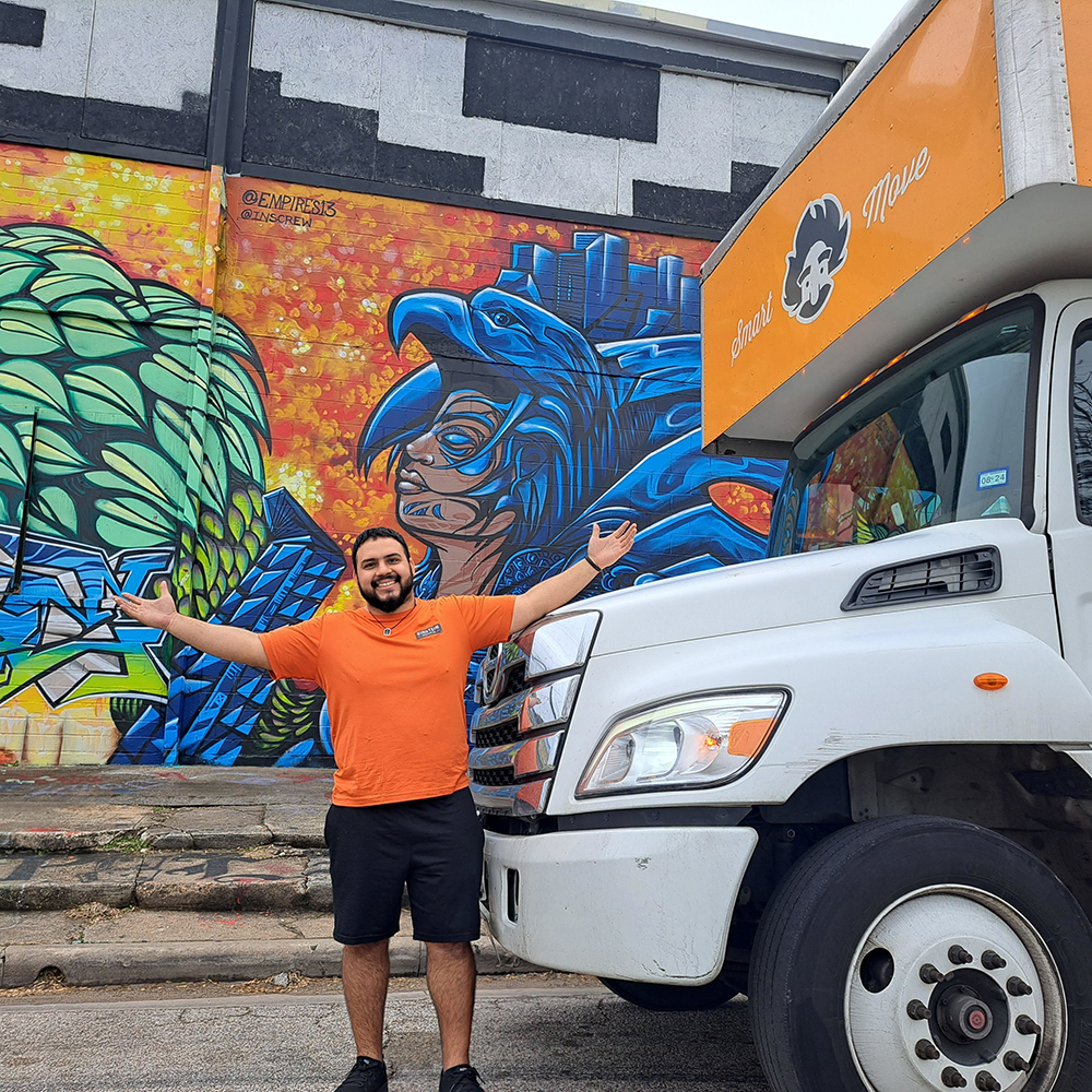 An Einstein mover stands in front of an Einstein moving truck which is parked in front of a colourful mural