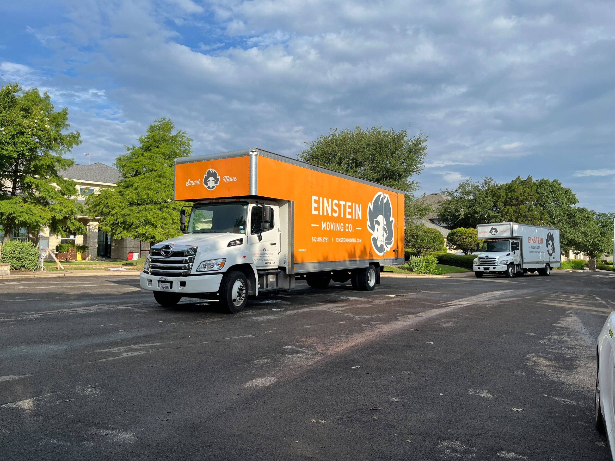 Two Einstein Moving trucks driving down a residential street. 